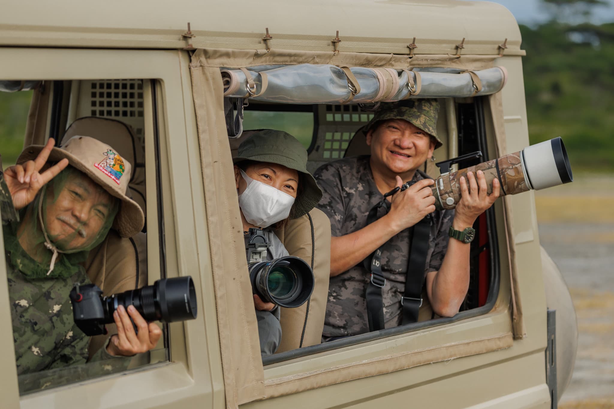 Tour guests with cameras ready, smiling from inside the safari vehicle