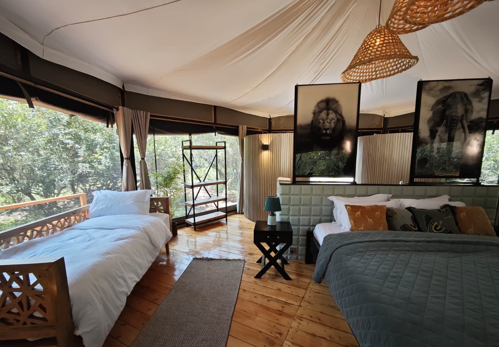 Interior of a luxury safari tent with twin beds, wooden floors, and wildlife artwork on the walls