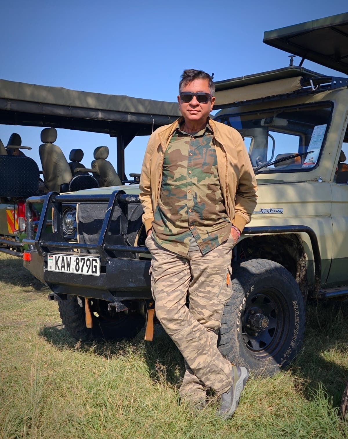 Nitin Vyas standing by a safari Land Cruiser on the Masai Mara savanna