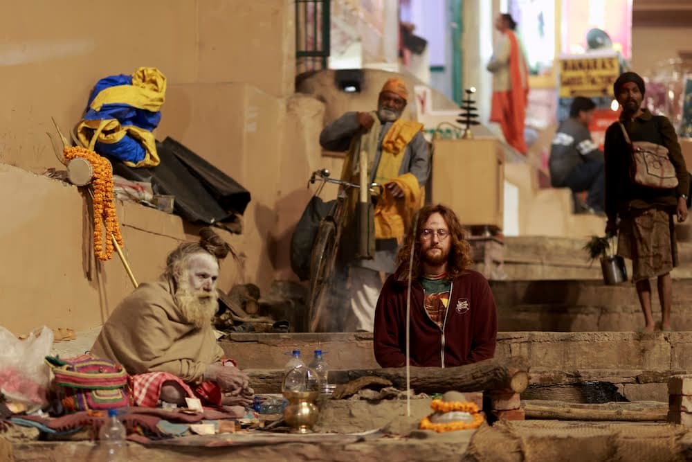 A sadhu and a traveller sitting together on the steps of a Varanasi ghat at night
